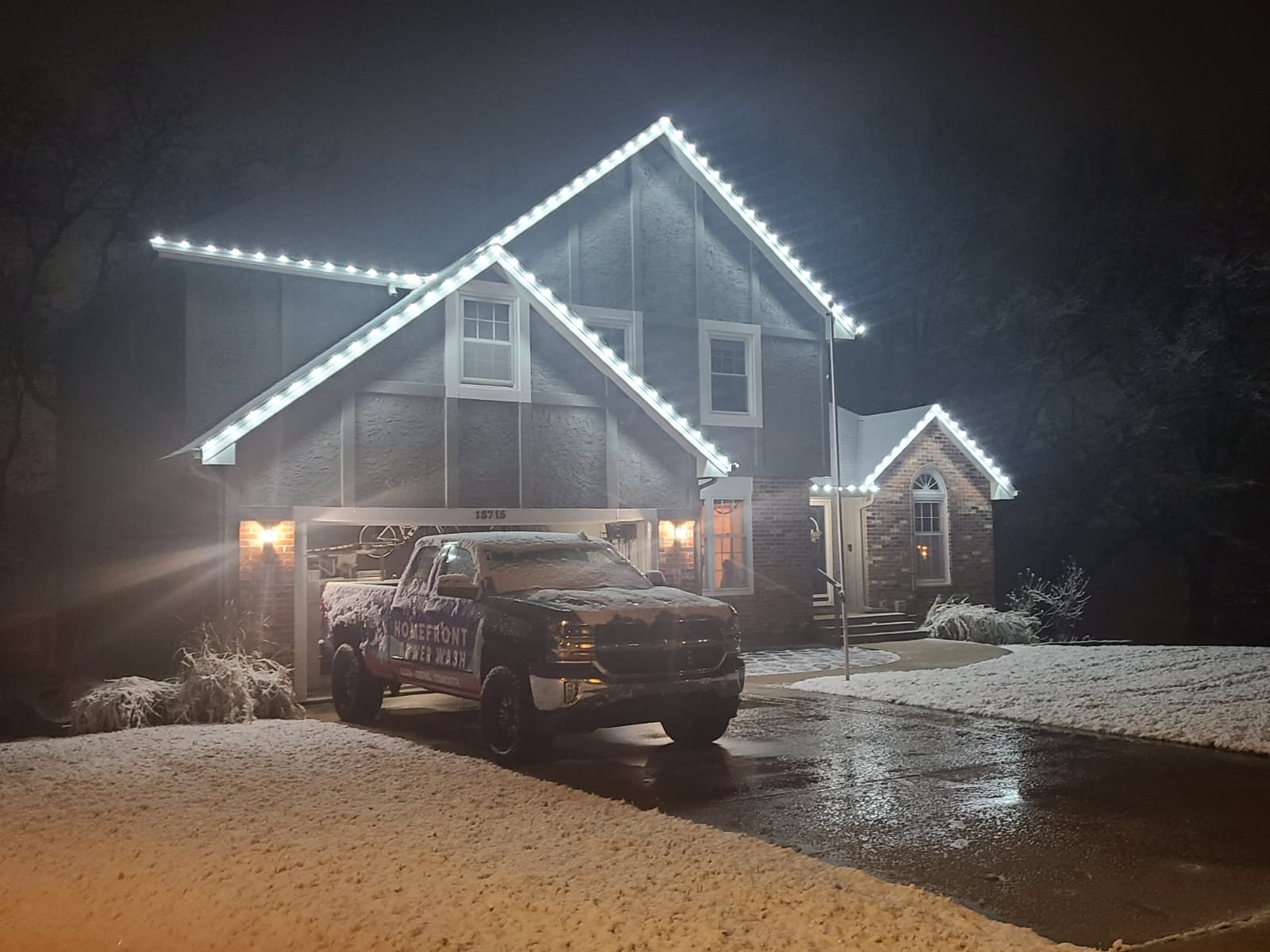 Home at night with roofline lighting reflecting off a wet driveway