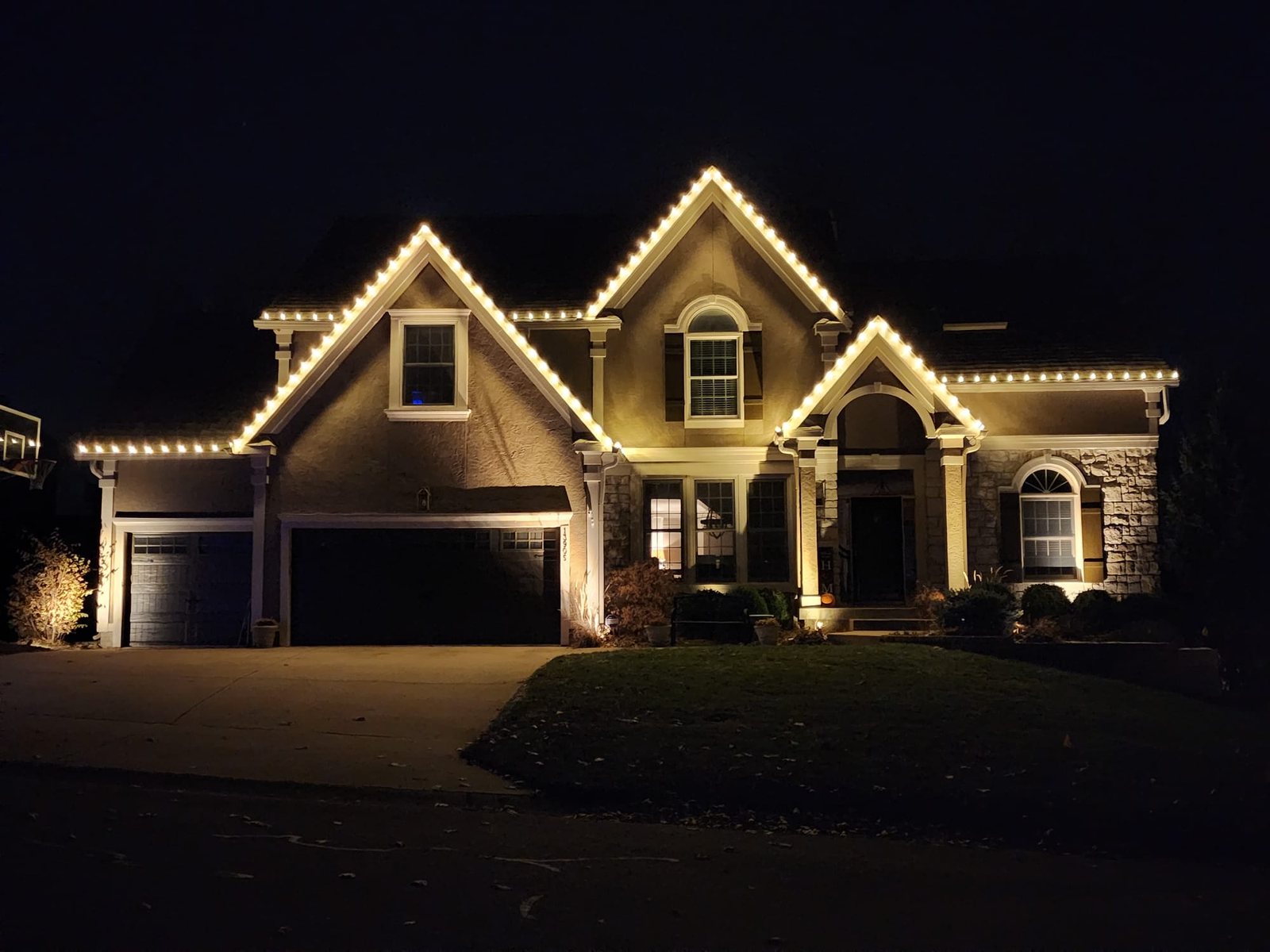 Large two-story home with warm white lighting along every roofline and gable