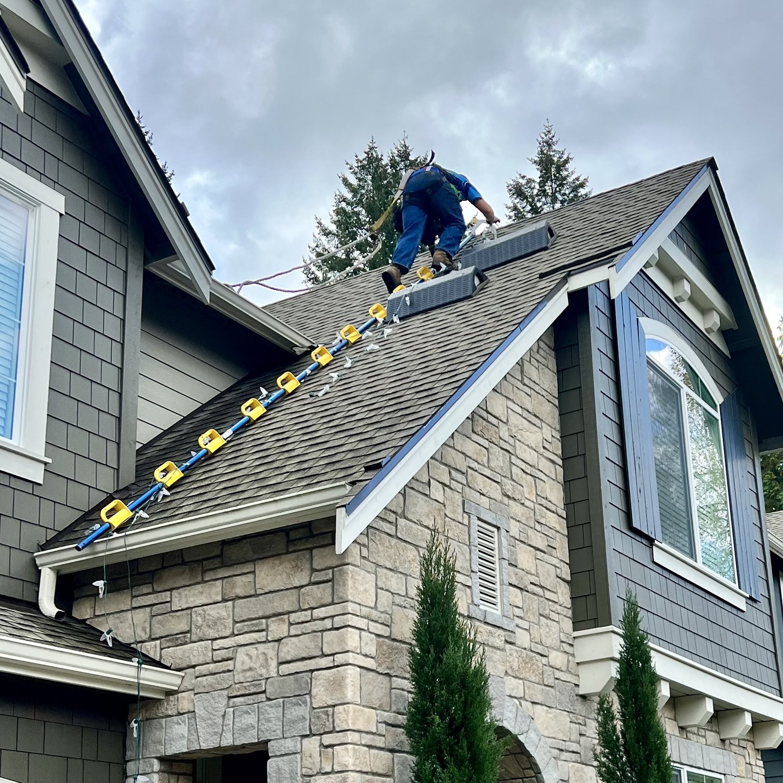 Installer working along the ridge of a shingled roof fitting lighting