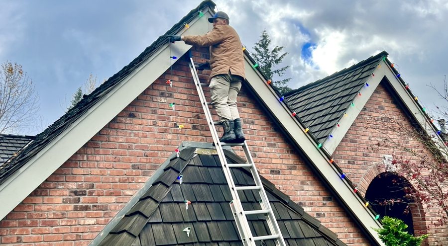 Installer on a ladder working along the roofline of a brick home