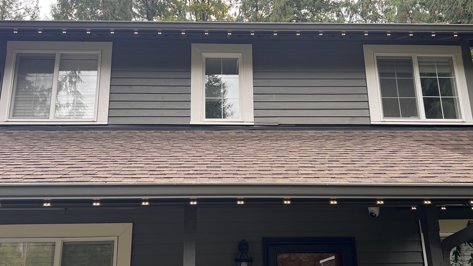 Gray home in daylight with permanent lighting track along the eaves, set to warm white